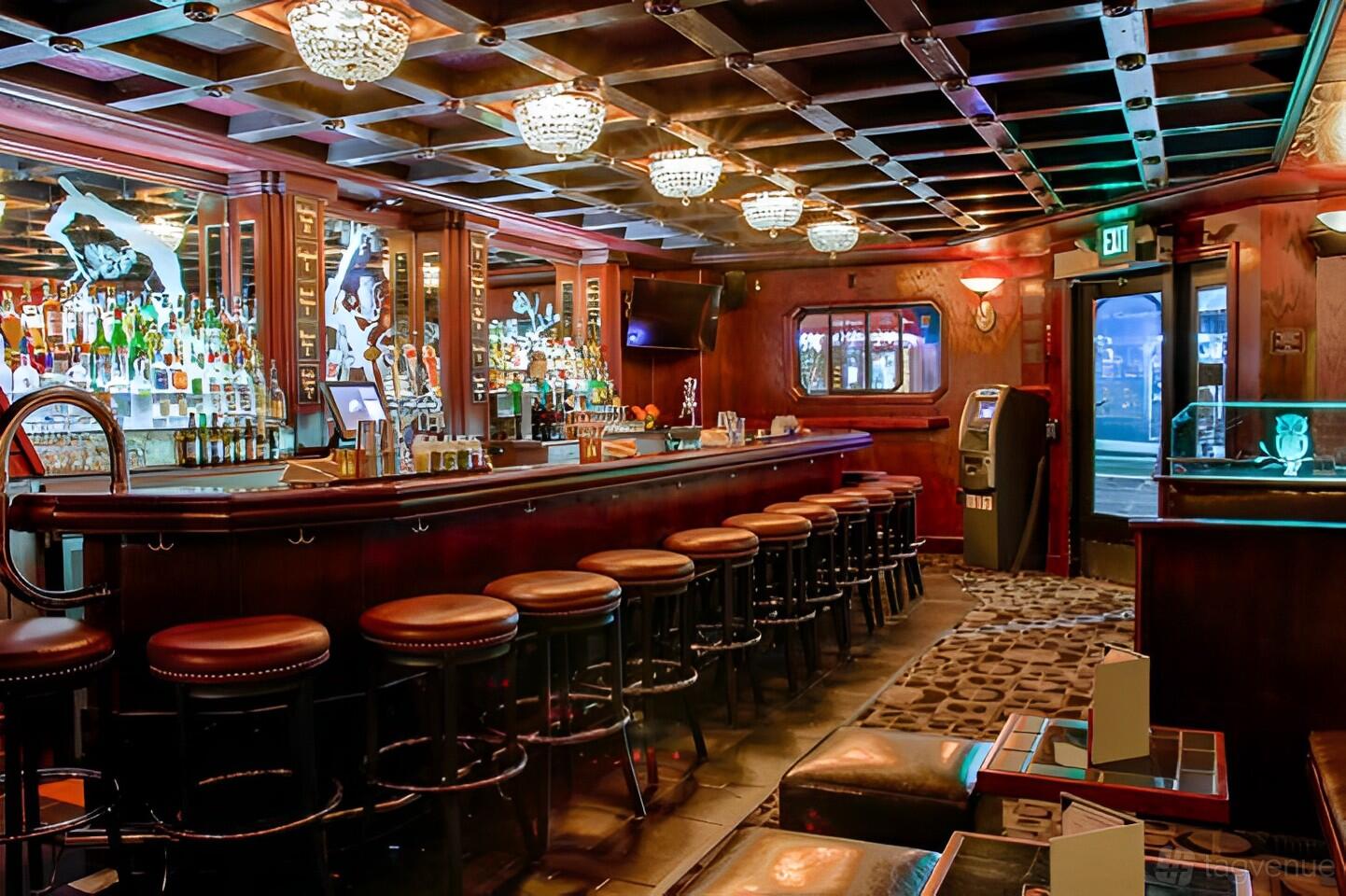 A cocktail bar with a long wooden bar, mirrored shelves of liquor, padded stools, and crystal ceiling lights at Owl Tree.