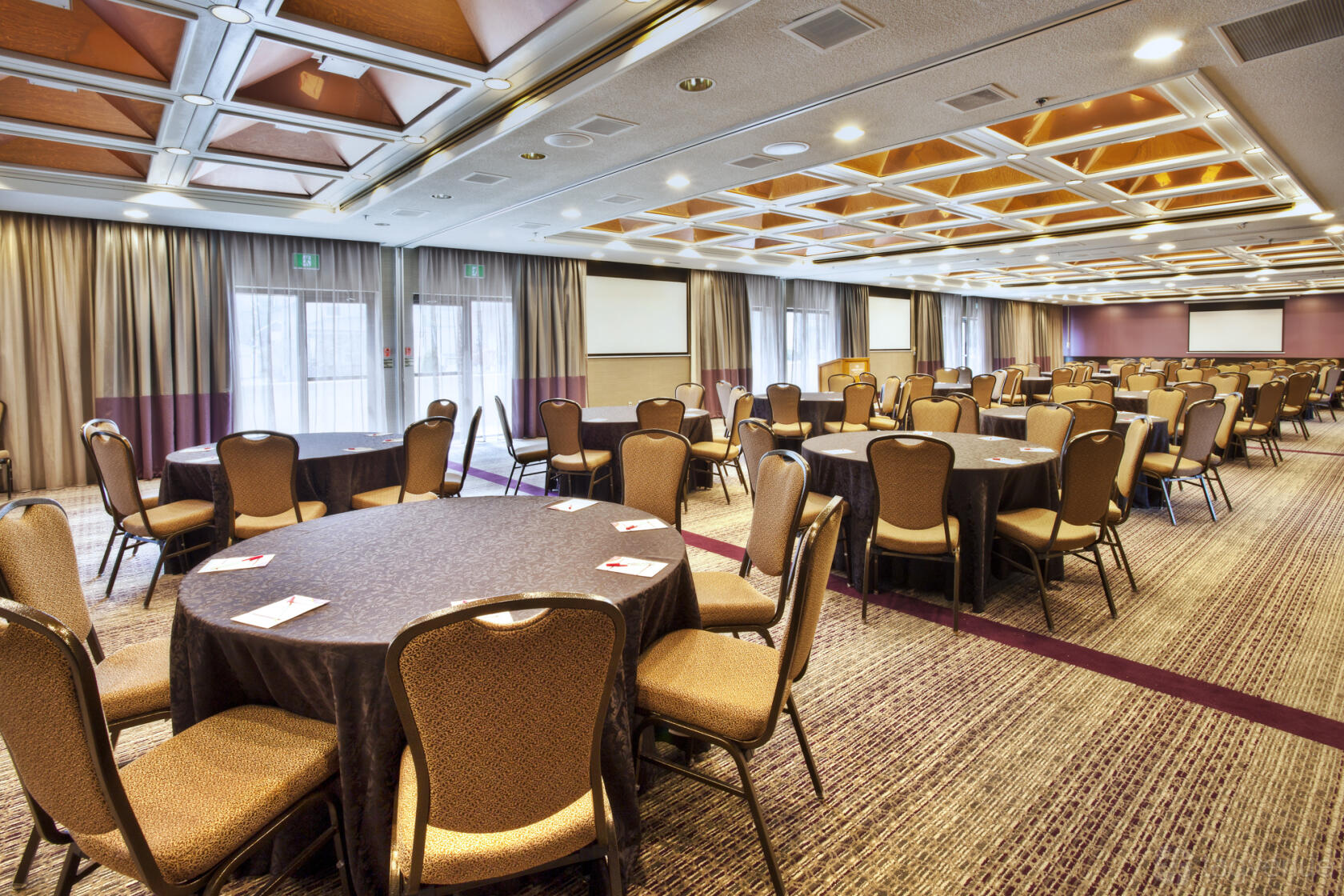 An event space with round tables draped in brown linens and natural light at CROWNE PLAZA KITCHENER-WATERLOO.