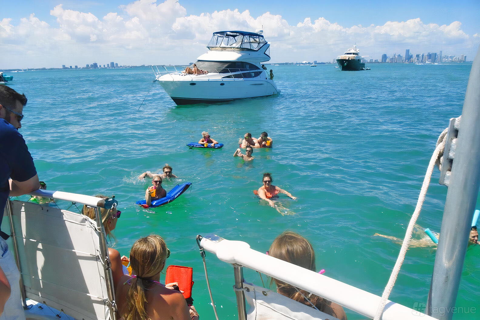 A party boat with an open deck and groups swimming nearby in clear blue water at Capt Nicks Miami Charters.