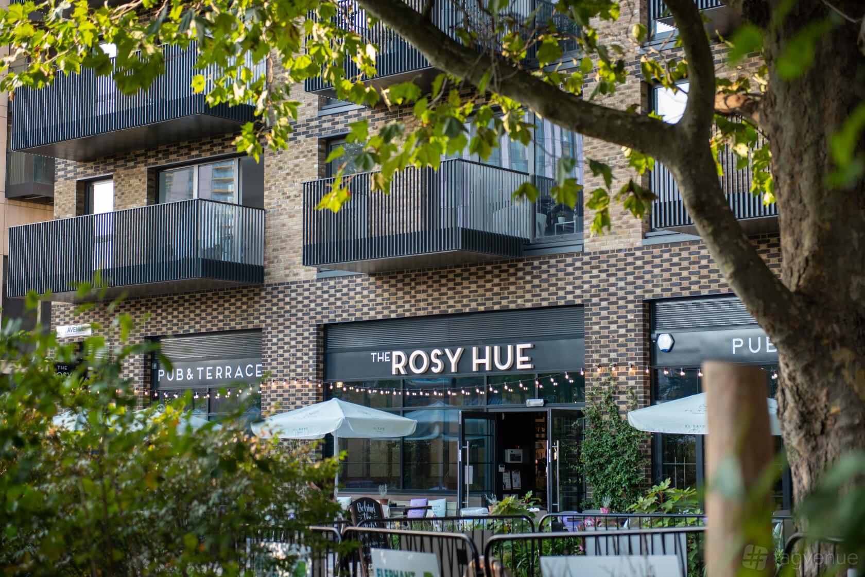 A pub with string lights, outdoor tables, and large umbrellas on the terrace at The Rosy Hue.