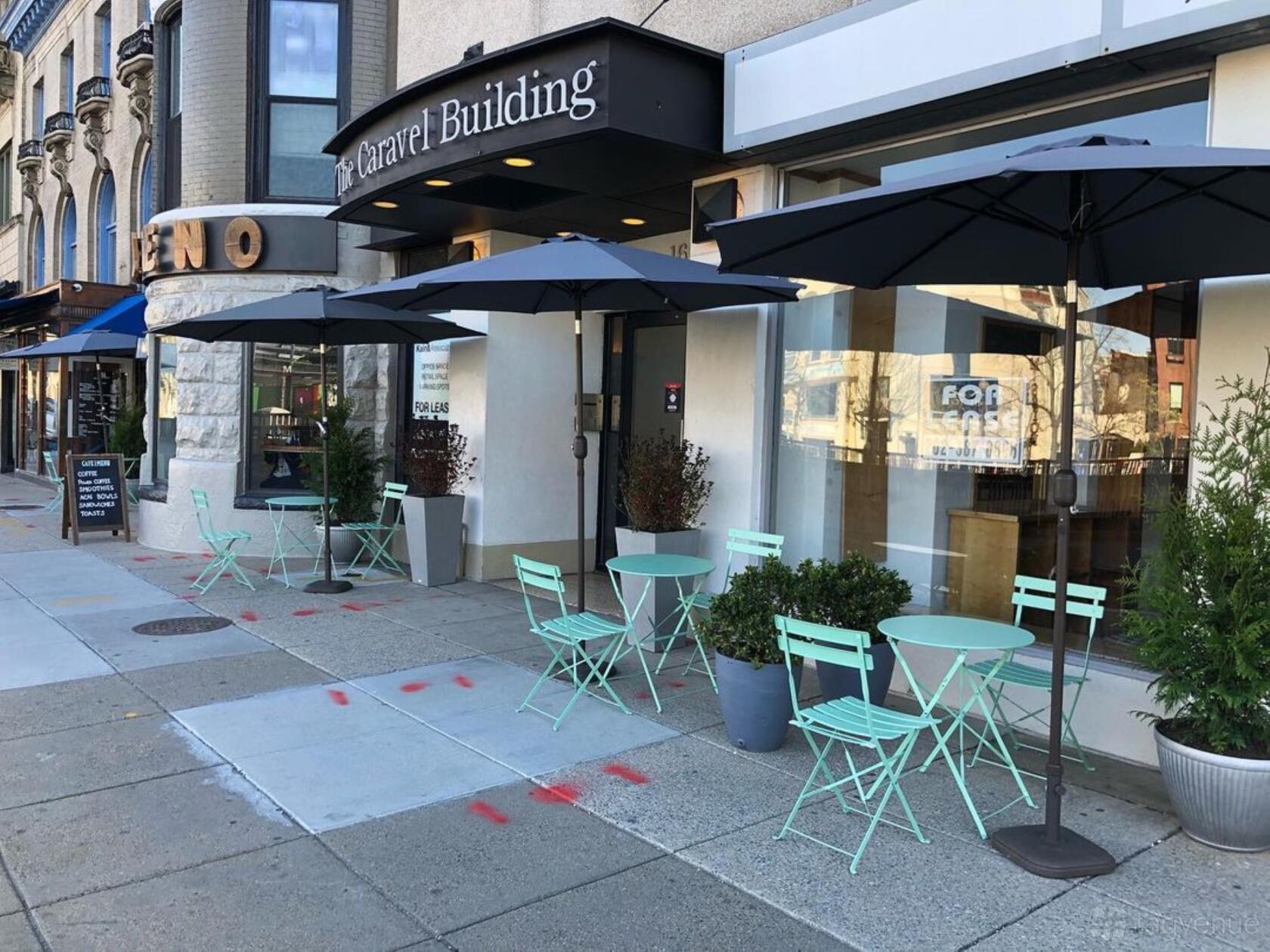 A café with mint green bistro tables, folding chairs, and black patio umbrellas on the sidewalk at Zeleno.