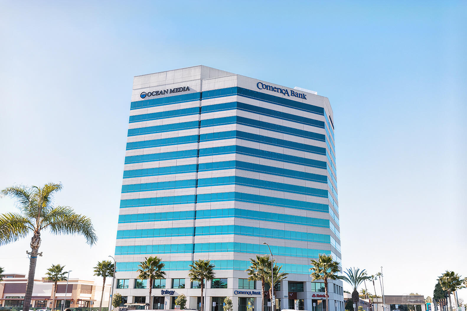 An office building with mirrored glass windows and palm trees at Premier Workspaces - Huntington Beach.