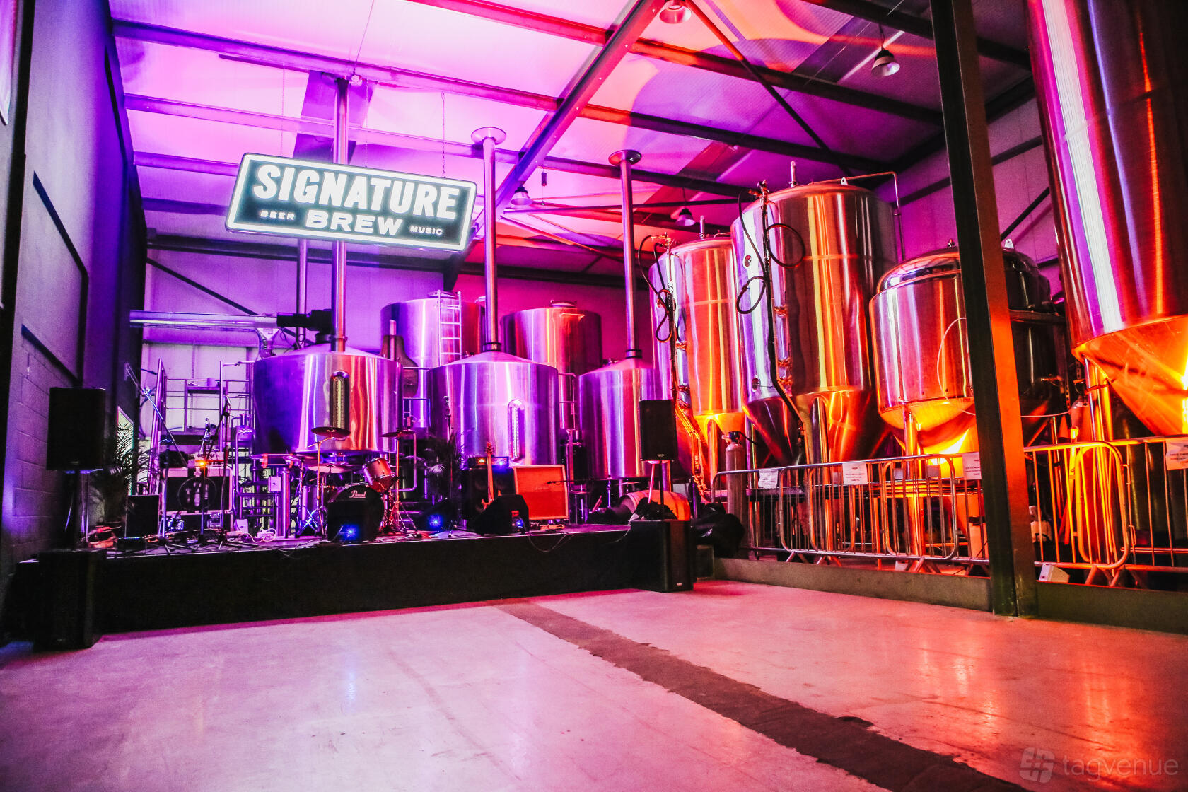 A brewery hall with large stainless steel brewing tanks, stage setup, and neon lighting at Signature Brew Blackhorse Road.