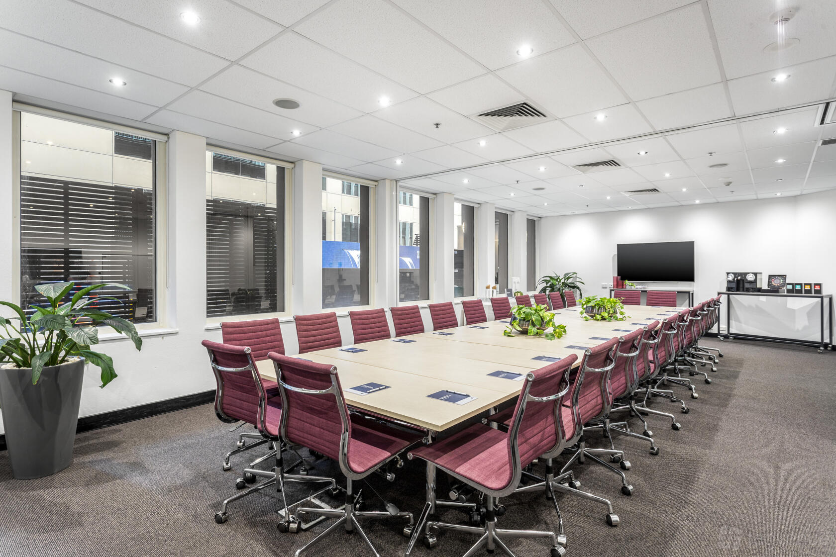 A boardroom in an office space with a long conference table, red swivel chairs, and wall-mounted television at Collins Street Tower.