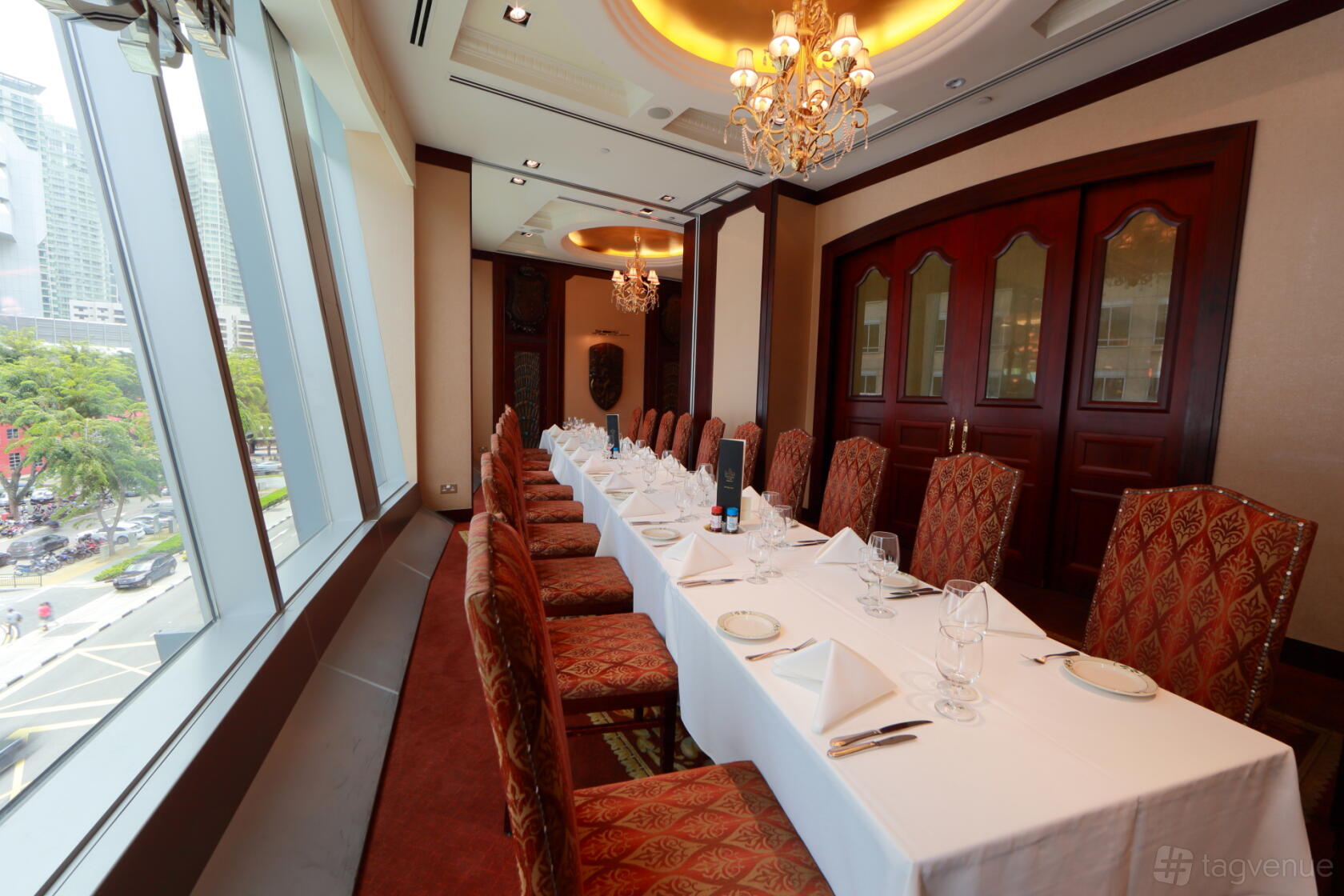 A dining room with a long table set with white linens, high-backed chairs, chandeliers, and large windows at Lawry's The Prime Rib.