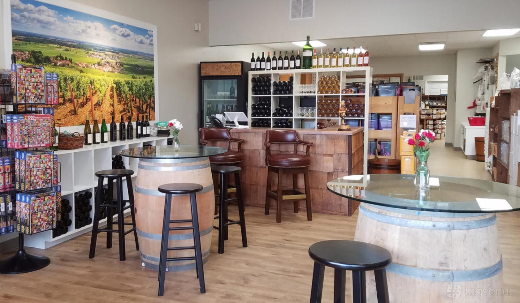 A winery with barrel tables, glass tops, wine bottle displays, and wood flooring at Beer & Wine Craft.