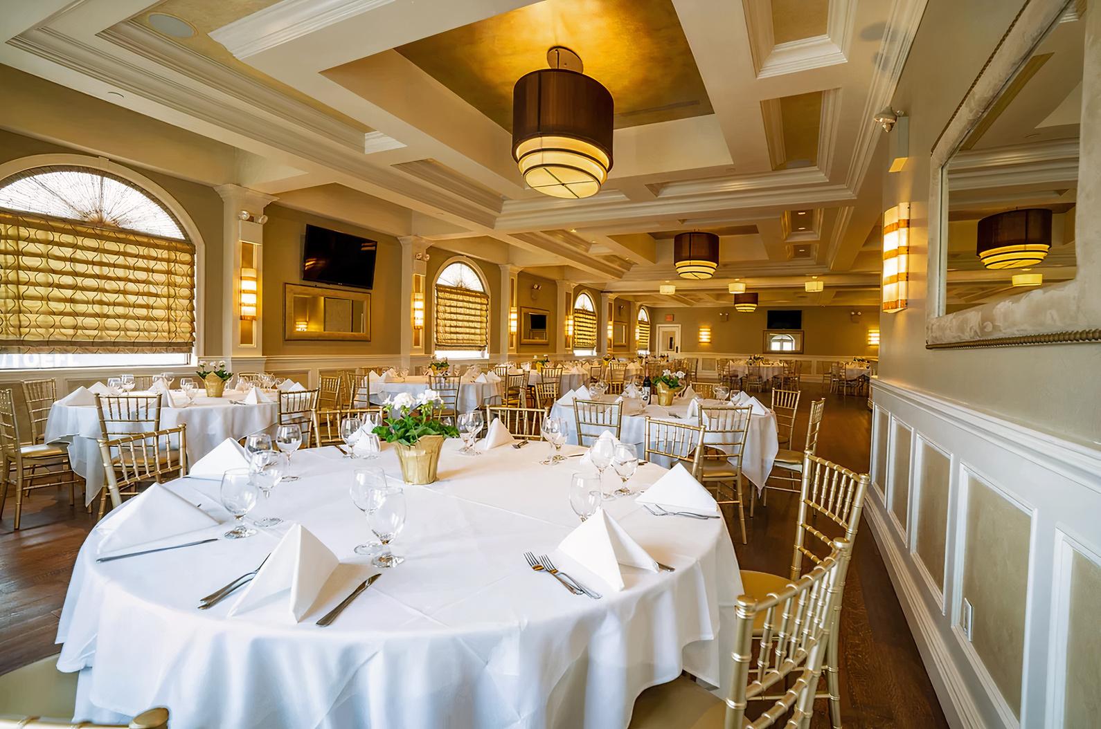 An event space in a restaurant with large windows, chandeliers, and round tables set with white linens at Il Bacco.