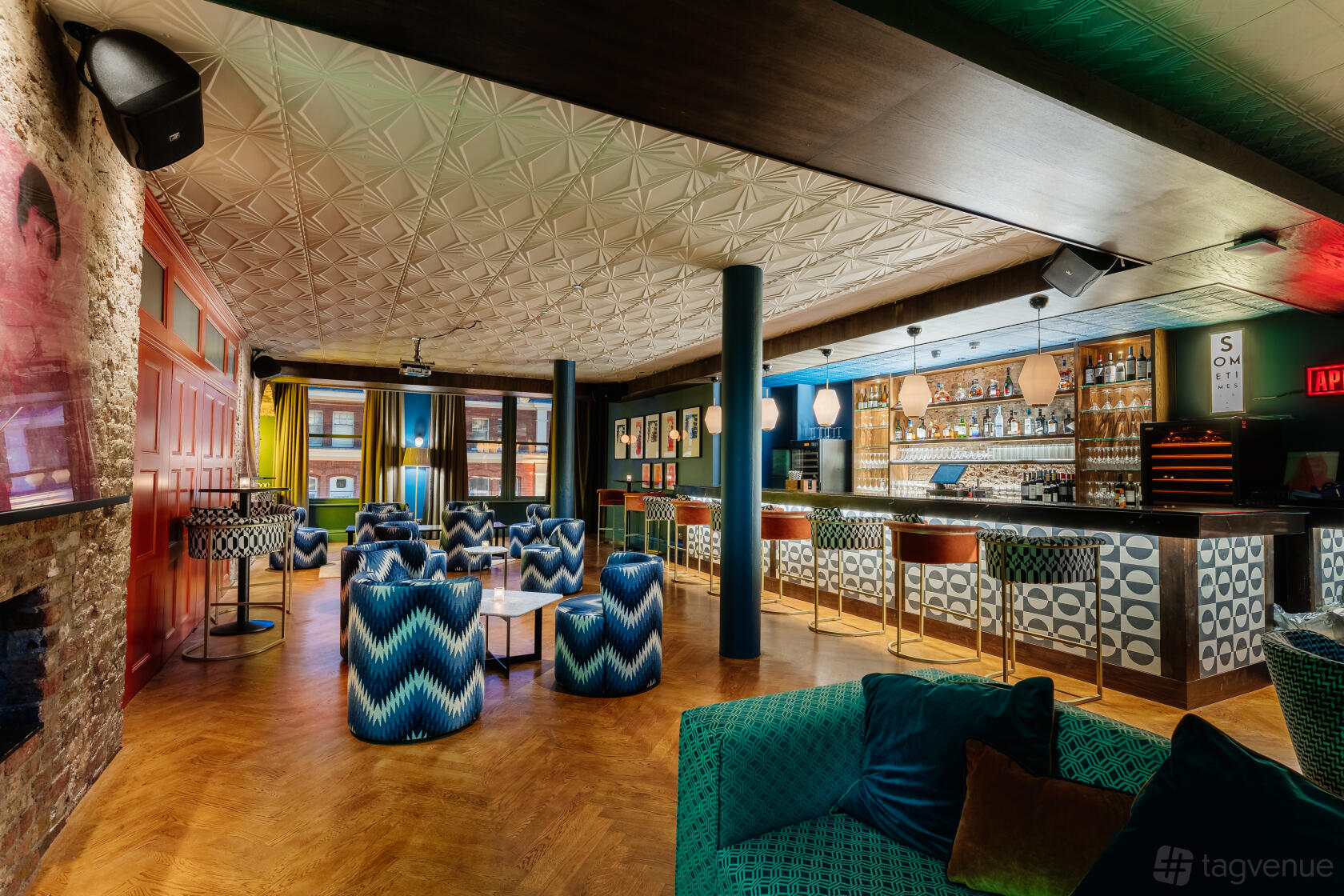 A cocktail bar with patterned upholstered chairs, geometric bar front, and backlit shelves at Century Club.