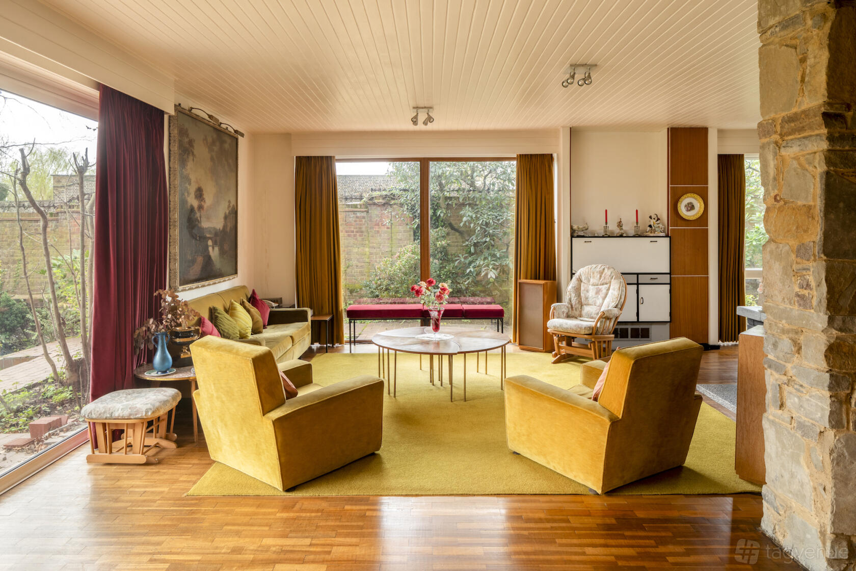 A living room with mustard armchairs, wood panel floors, and floor-to-ceiling windows at Iconic Mid-century London House. 50's / 60's.