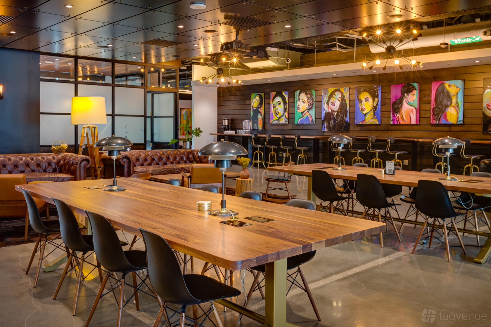 An event space with long wooden tables, black chairs, leather sofas, and colorful portraits on the wall at Venture X LoDo.