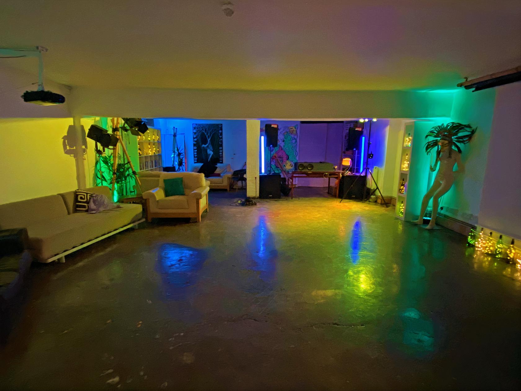 An event space in a nightclub with colorful LED lighting, DJ booth, couches, and art displays at Dalston Den.