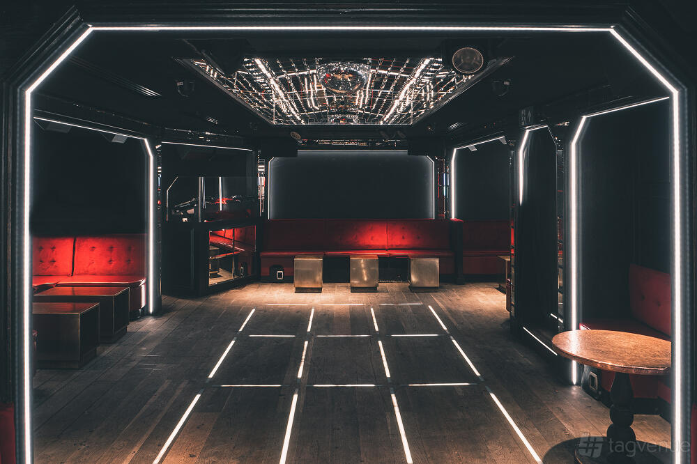 A nightclub with red velvet banquette seating, illuminated floor strips, and a mirrored ceiling at The Scotch of St James.