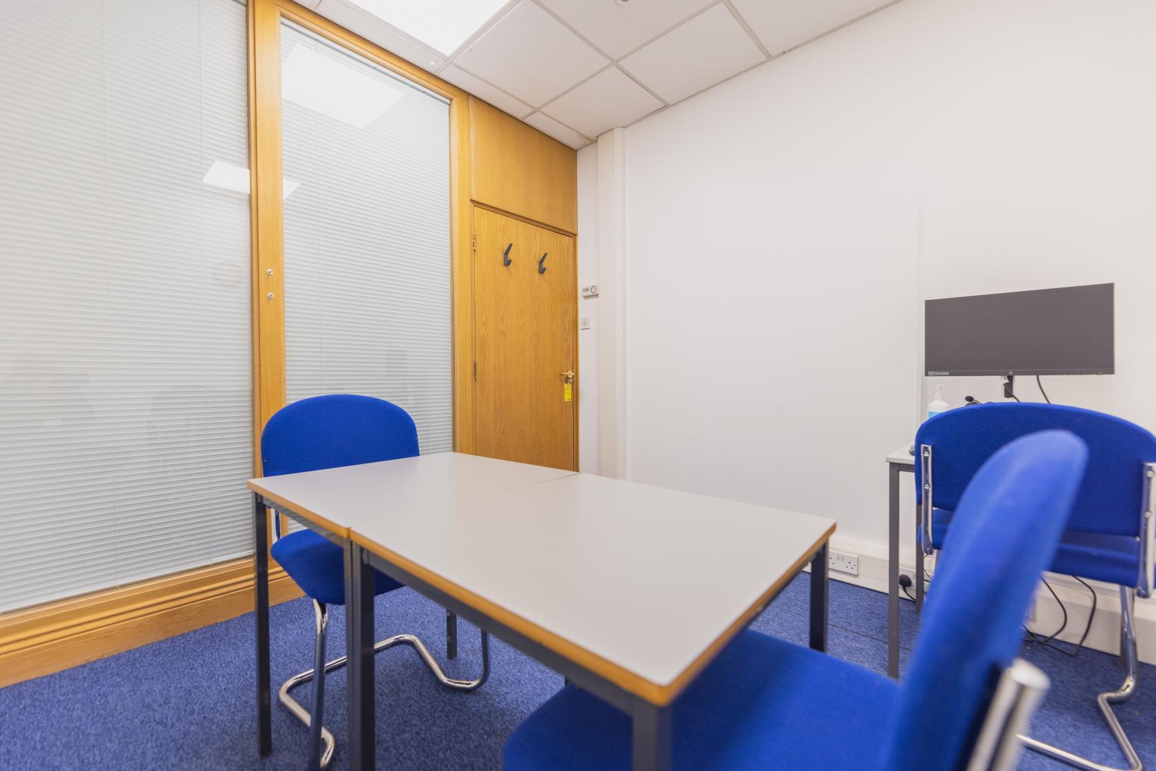 A meeting room with a rectangular table, blue chairs, and a wall-mounted monitor at University of Law - Birmingham.