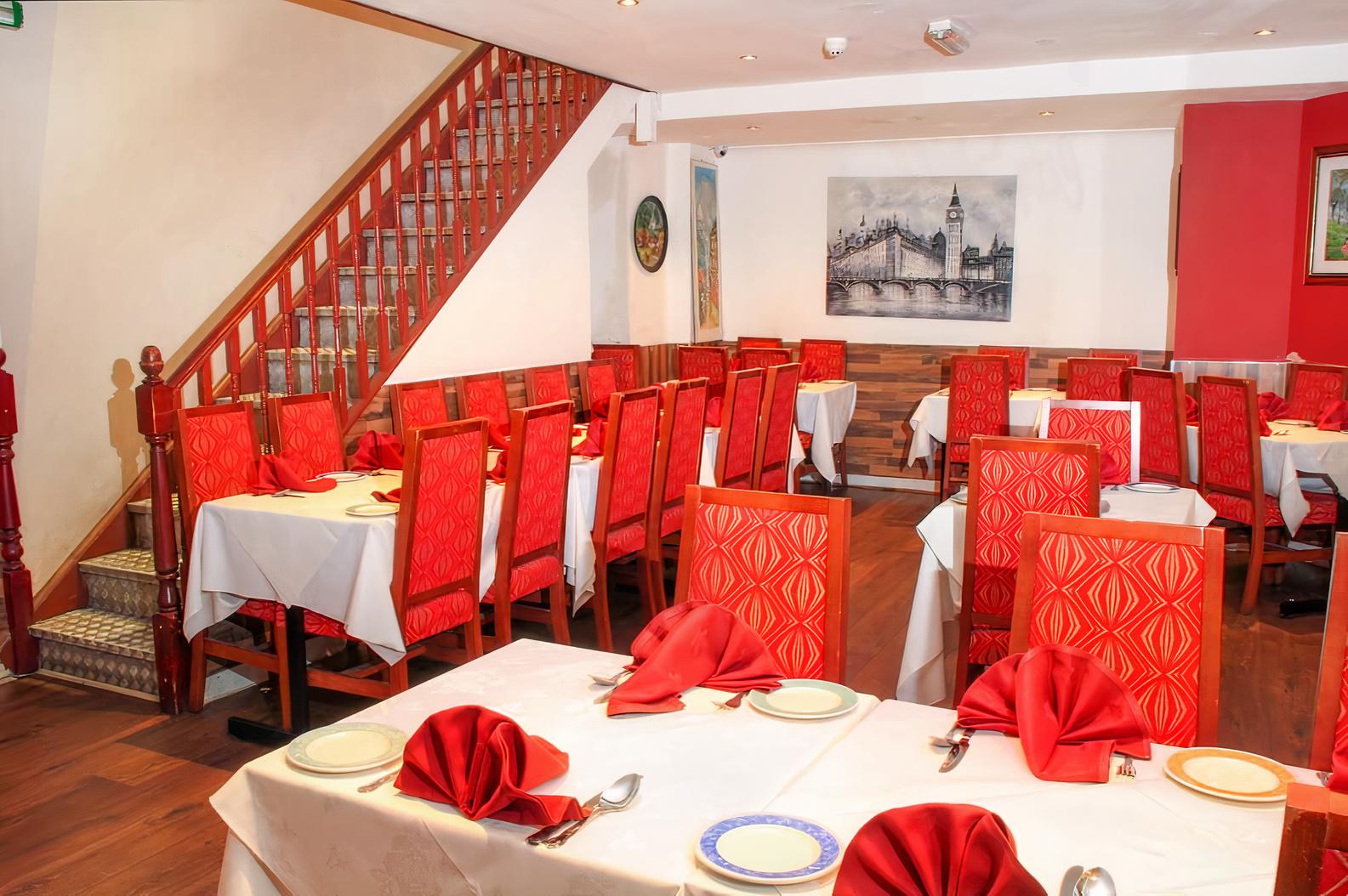 A restaurant with red upholstered chairs, white tablecloths, and folded red napkins on tables at City Spice.