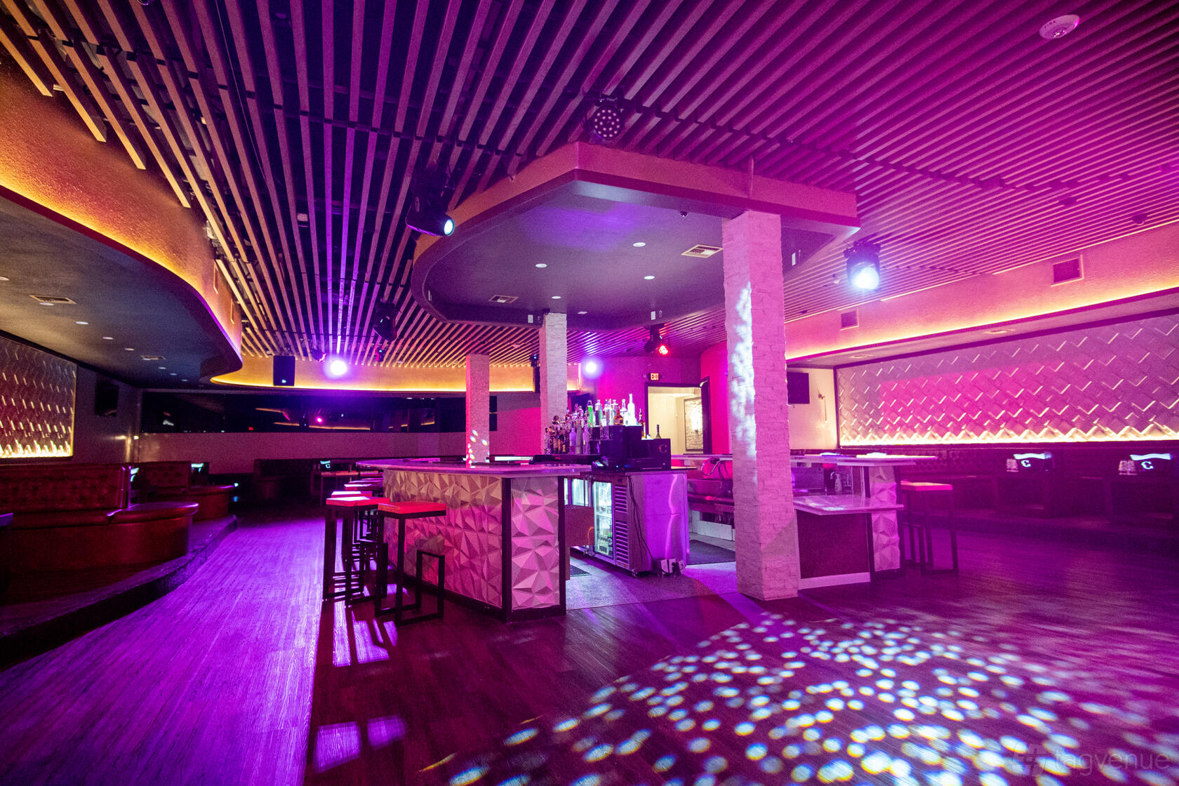 A bar with a central bar counter, colorful LED lighting, wood flooring, and booth seating at Da Cave Miami.