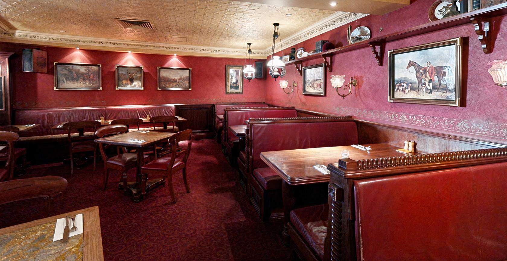 An event space in a bar with red leather booths, framed paintings, and decorative plates at Pig ‘N’ Whistle - Riverside.