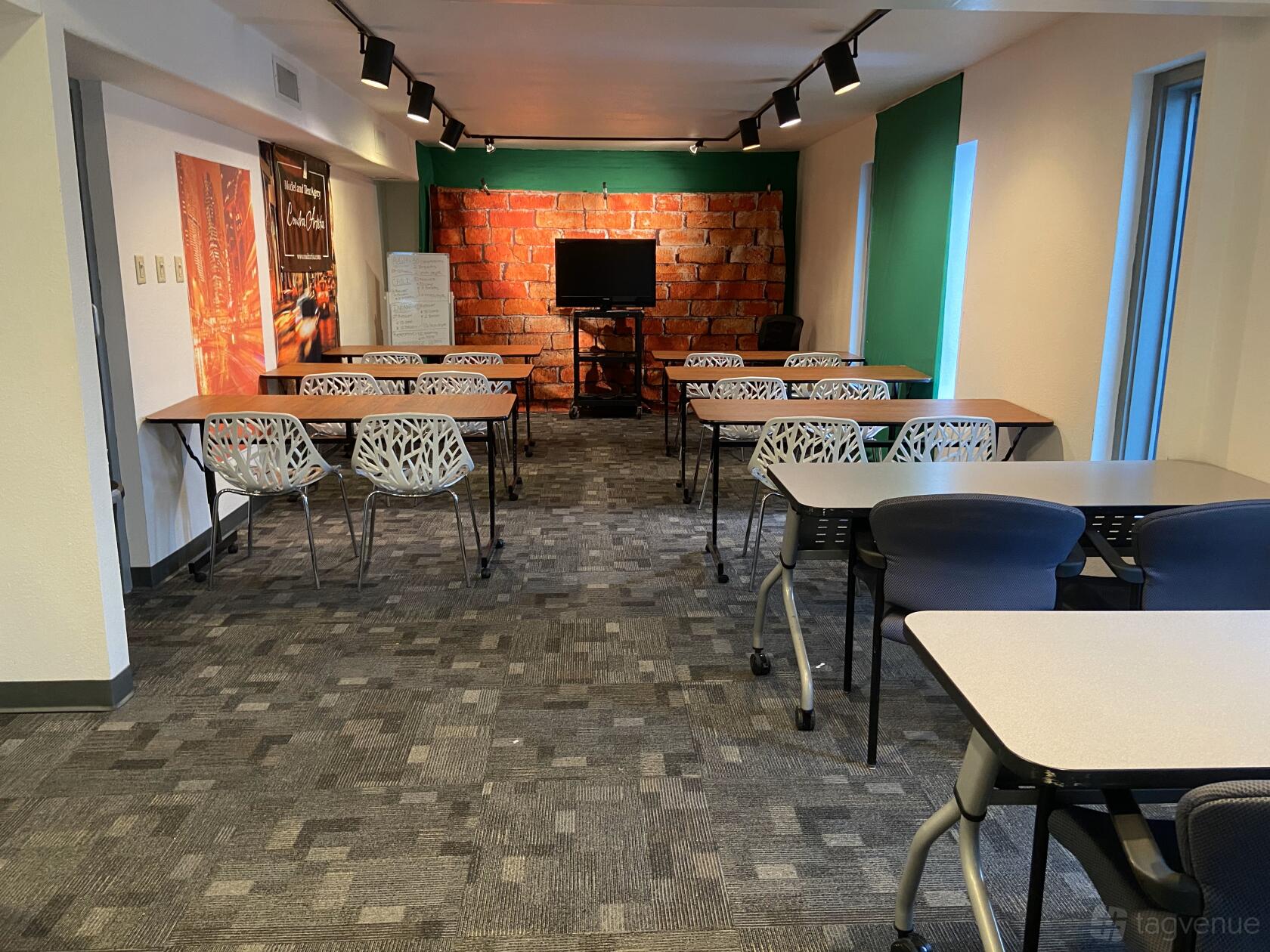 A meeting room with exposed brick accent wall, rows of tables, and modern chairs at Alamo City Studios.