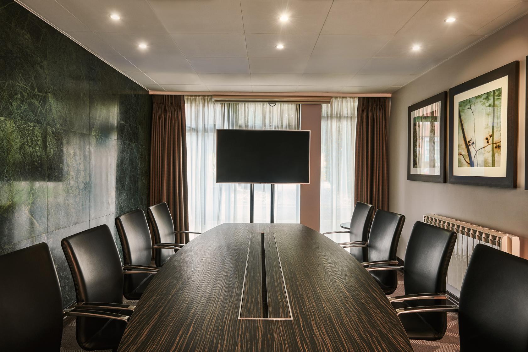 A hotel boardroom with a long wood table, leather chairs, wall art, and a large monitor at DoubleTree by Hilton London - Ealing.
