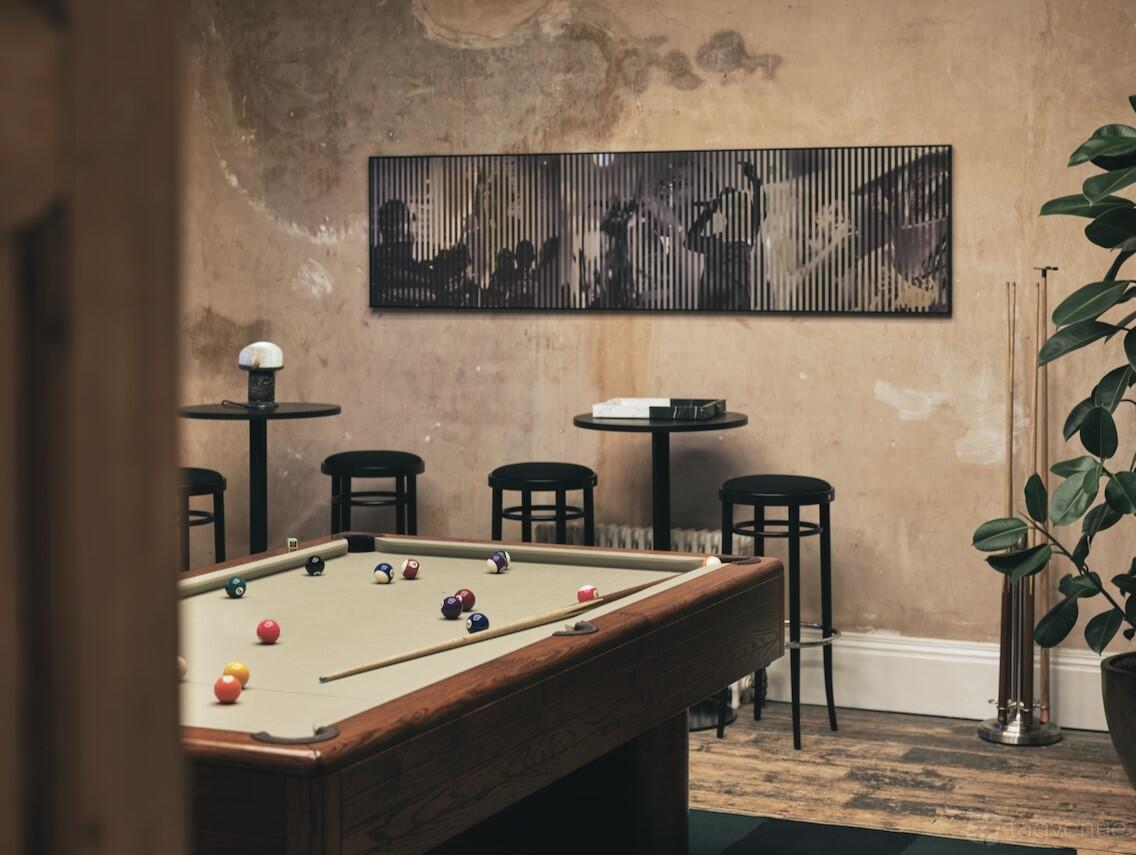 A rooftop terrace with a billiards table, high stools, round tables, and exposed plaster walls at Knotel at Old Sessions House.