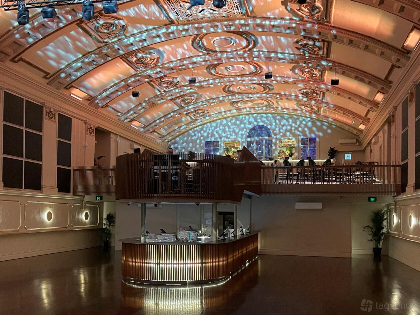 A theatre with an ornate arched ceiling, raised balcony, and illuminated central bar at Northcote Theatre.