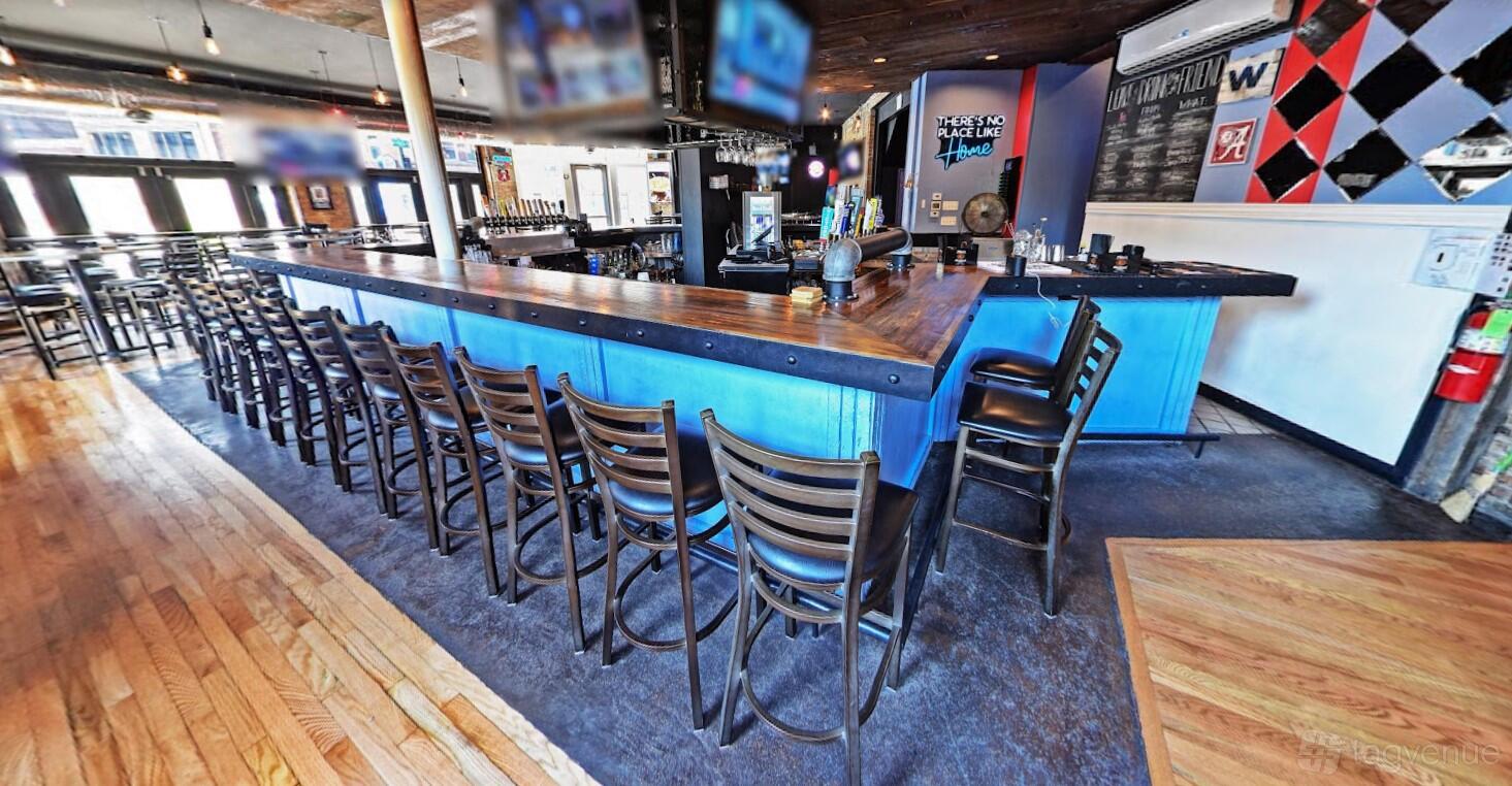 A bar with a long wooden counter, high-top chairs, and liquor shelves behind the bar at Almost Home Tavern & Grill.