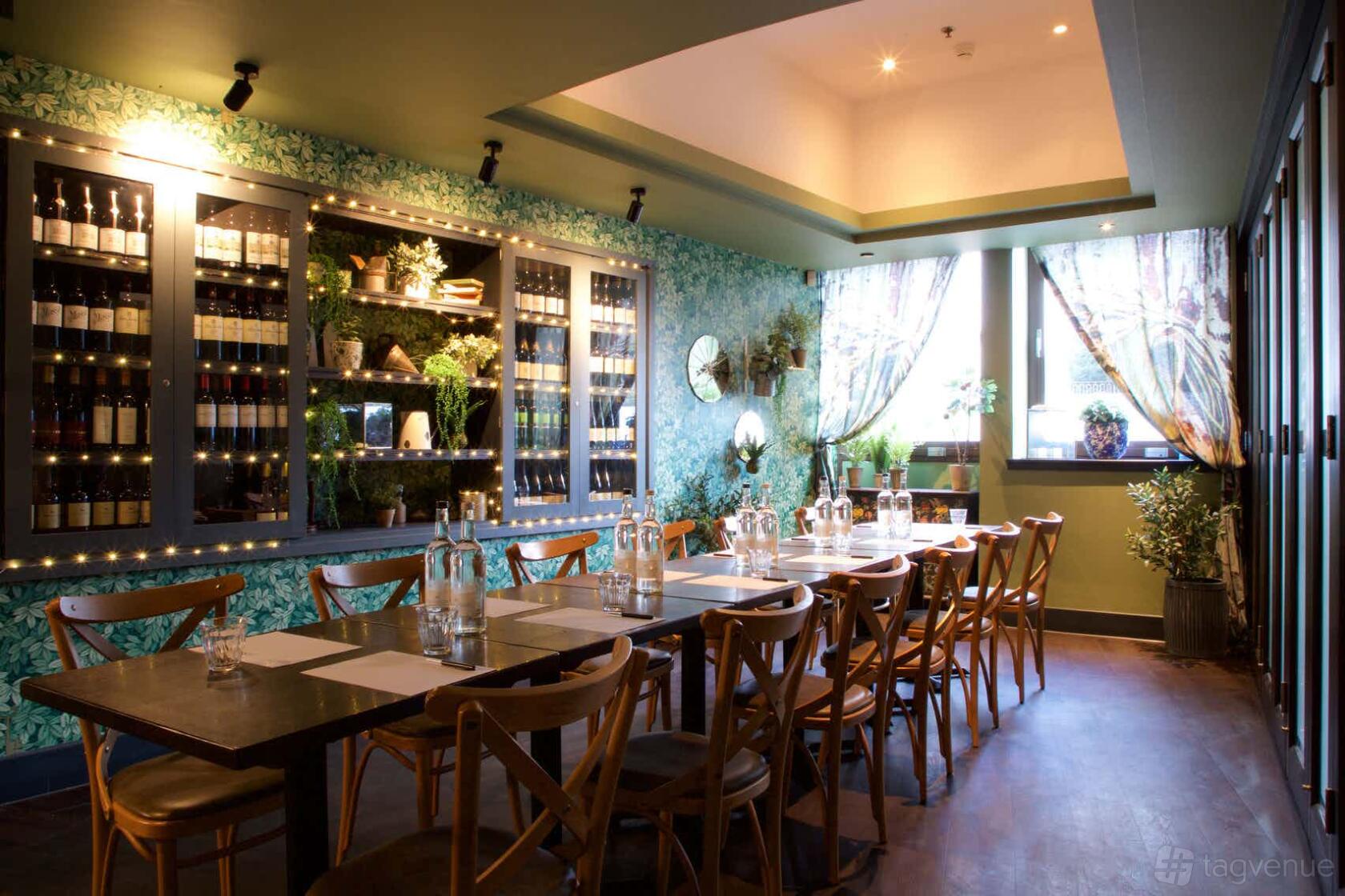 A private dining room with a long wooden table, cross-back chairs, wine display cabinets, and leafy wallpaper at Brasserie Blanc Southbank.