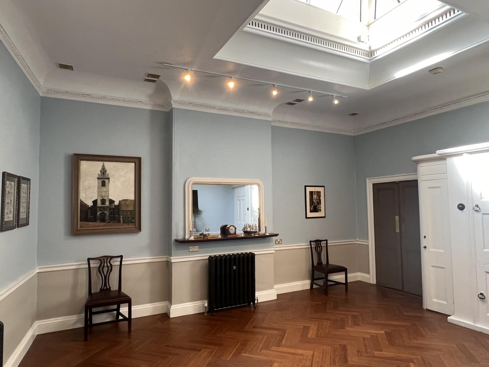 A church meeting room with parquet wood flooring, skylight, framed artwork, and classic wooden chairs at The Garlickhythe Rooms.
