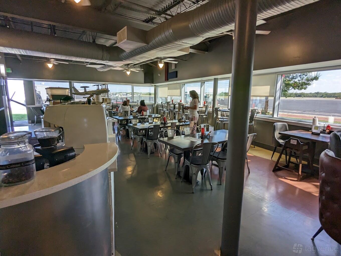 A restaurant with floor-to-ceiling windows, exposed ductwork, and metal dining tables at Trailblazer Café.