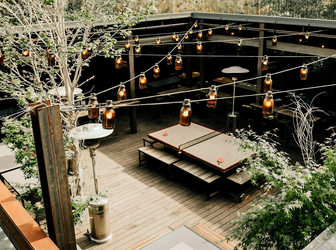 A pub terrace with wooden decking, picnic tables, trees, and hanging jar lights at The National Hotel.
