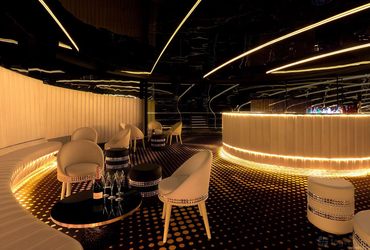 An event space in a nightclub with a curved illuminated bar, round lounge chairs, and patterned flooring at Bond Melbourne.