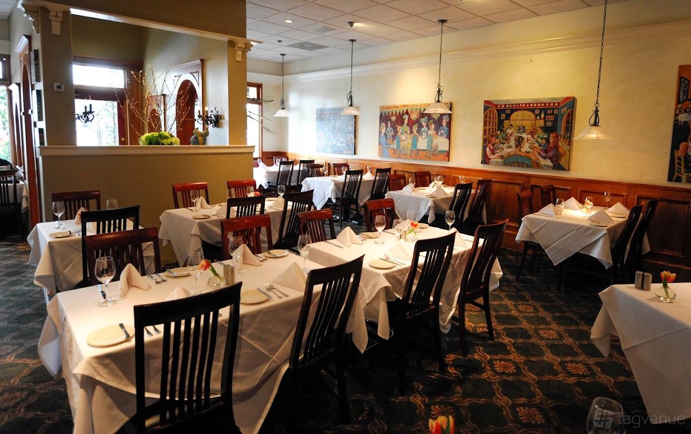 A restaurant dining room with white tablecloths, wooden chairs, framed artwork, and pendant lighting at Hunsakers.