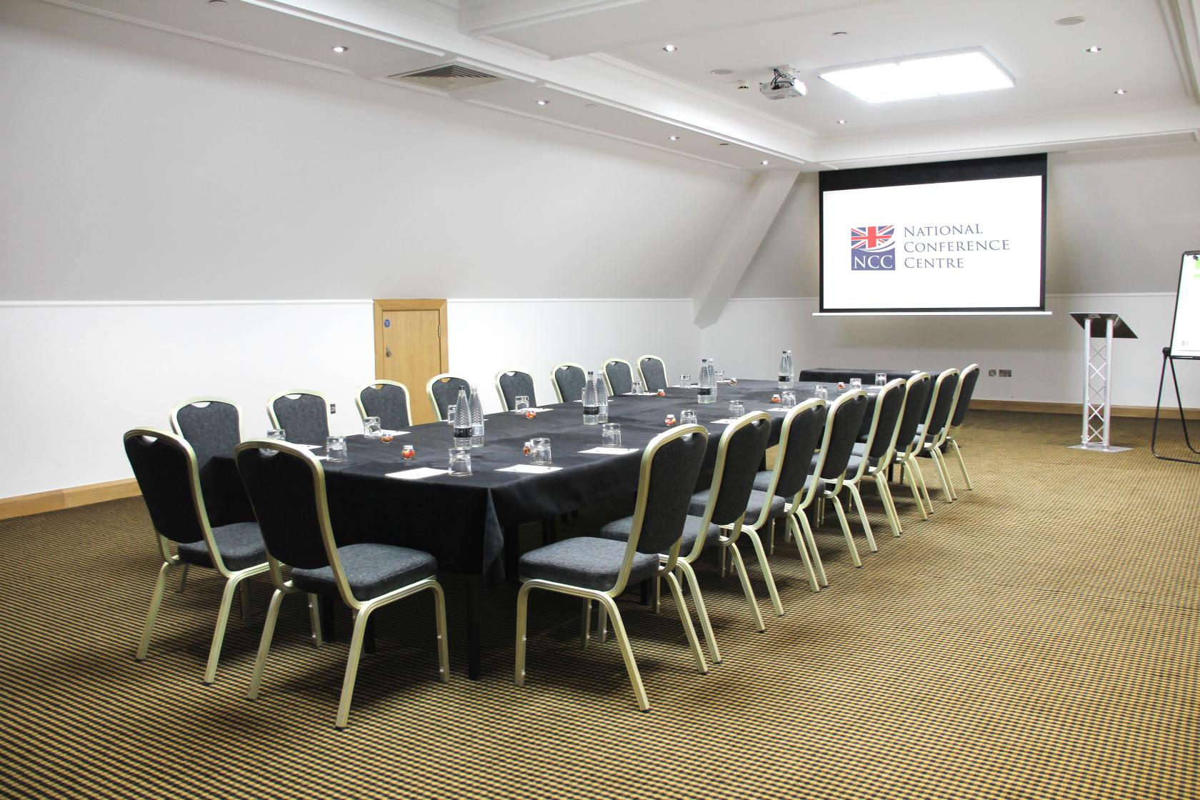 A meeting room with a U-shaped arrangement of chairs, projection screen, and natural skylight at National Motorcycle Museum.