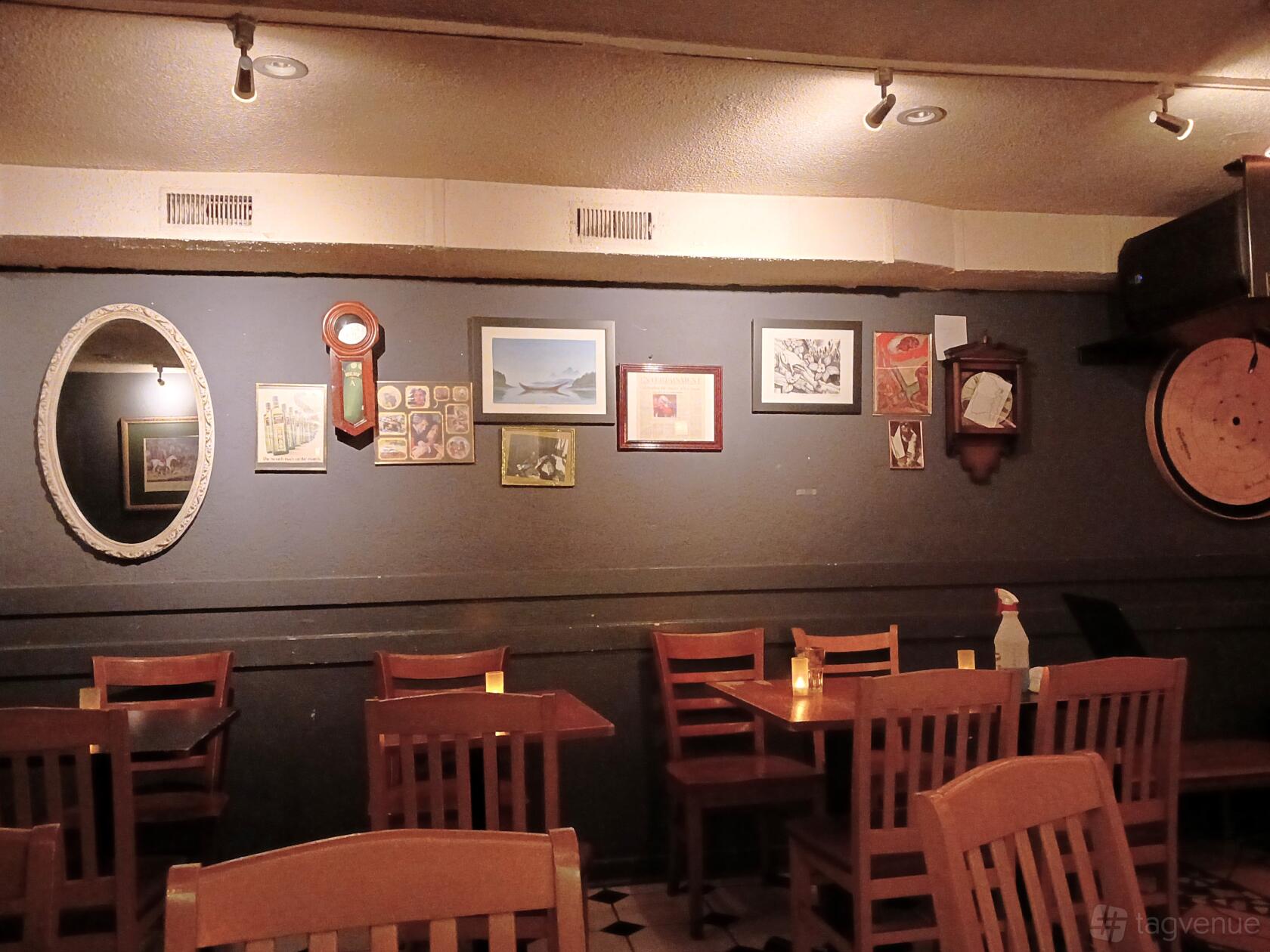 A bar with wooden tables, chairs, dim lighting, and vintage artwork on dark walls at The Emmet Ray.