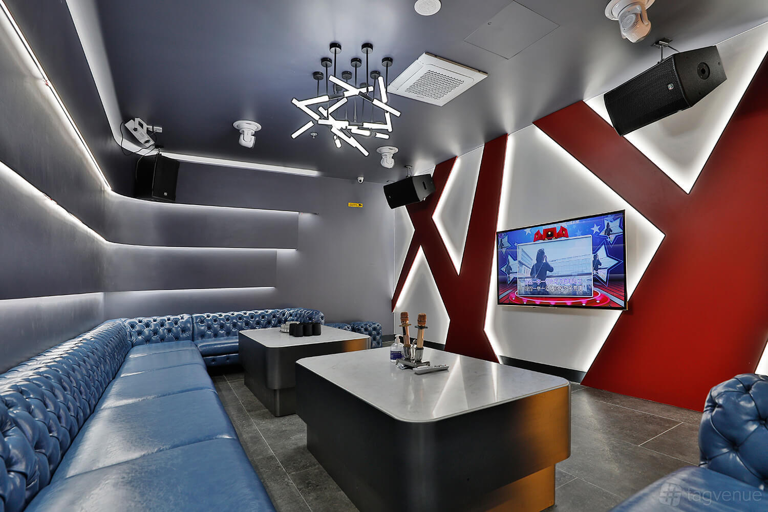A private karaoke room with tufted blue sofas, LED strip lighting, and a wall-mounted screen at Game Republic Karaoke Entertainment Centre.