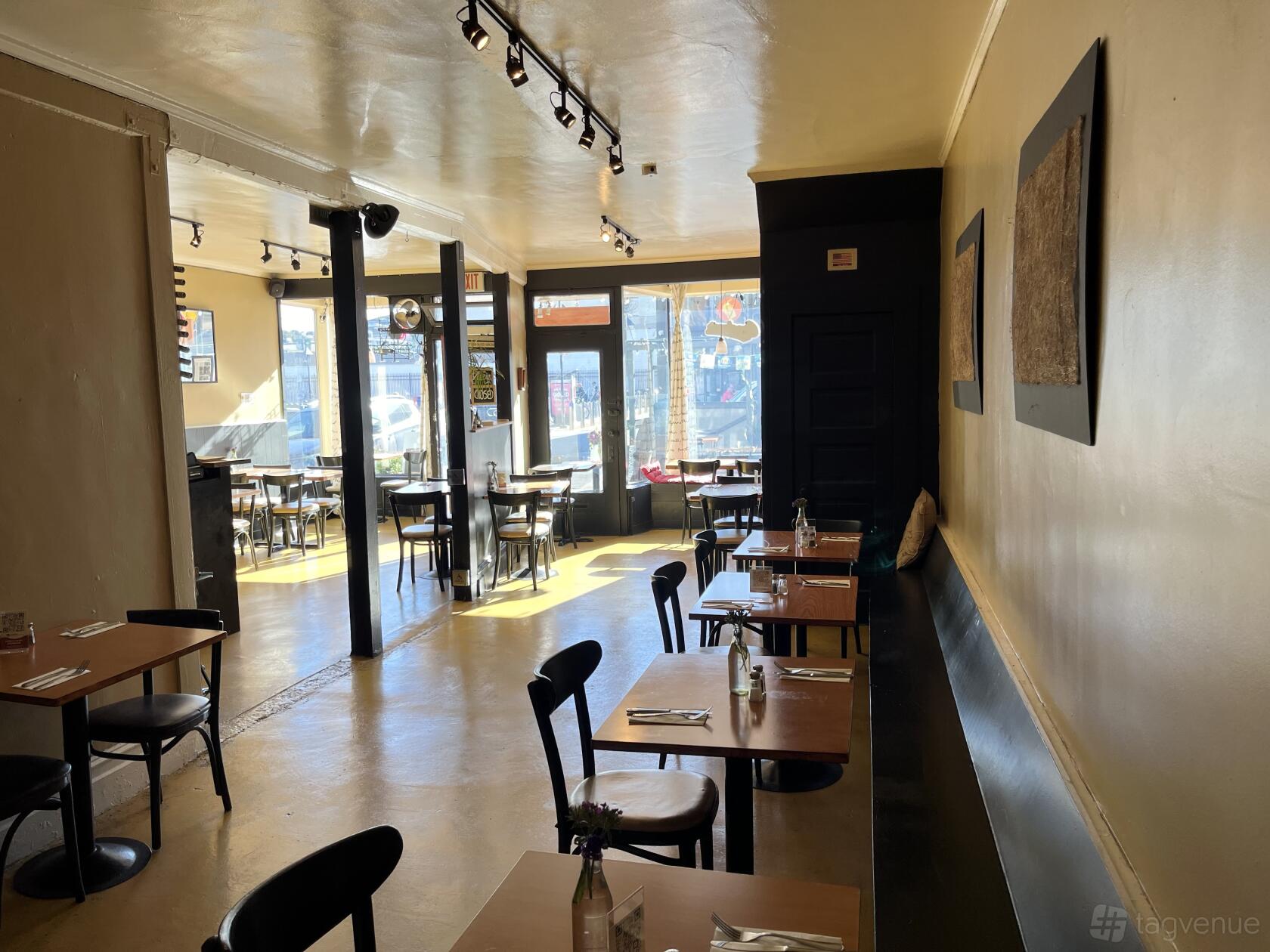 A restaurant with large front windows, wooden tables and black chairs at Paprika.