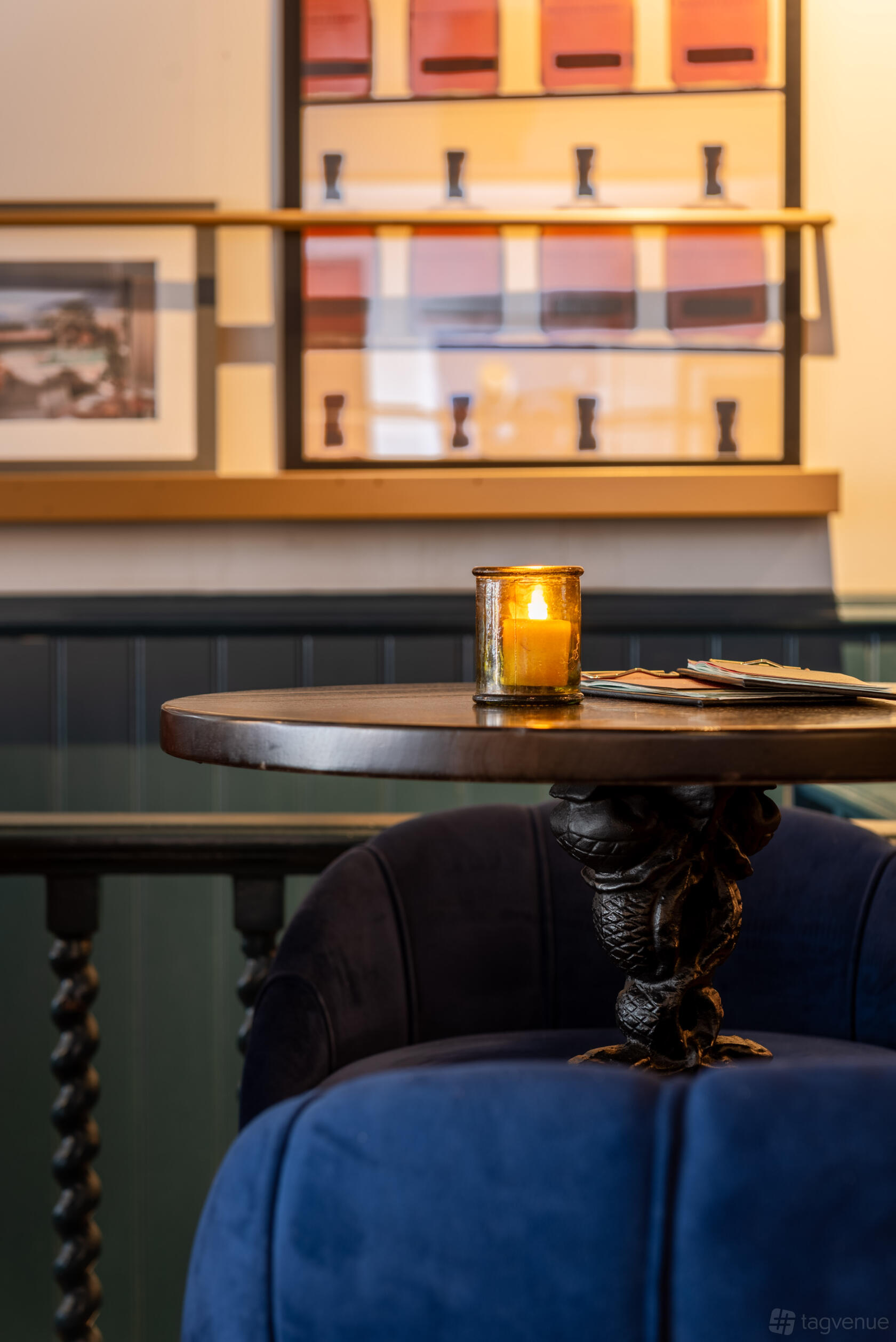 A cocktail bar event space with a round wooden table, lit candle, and upholstered chairs at LOCKES Bar Covent Garden.