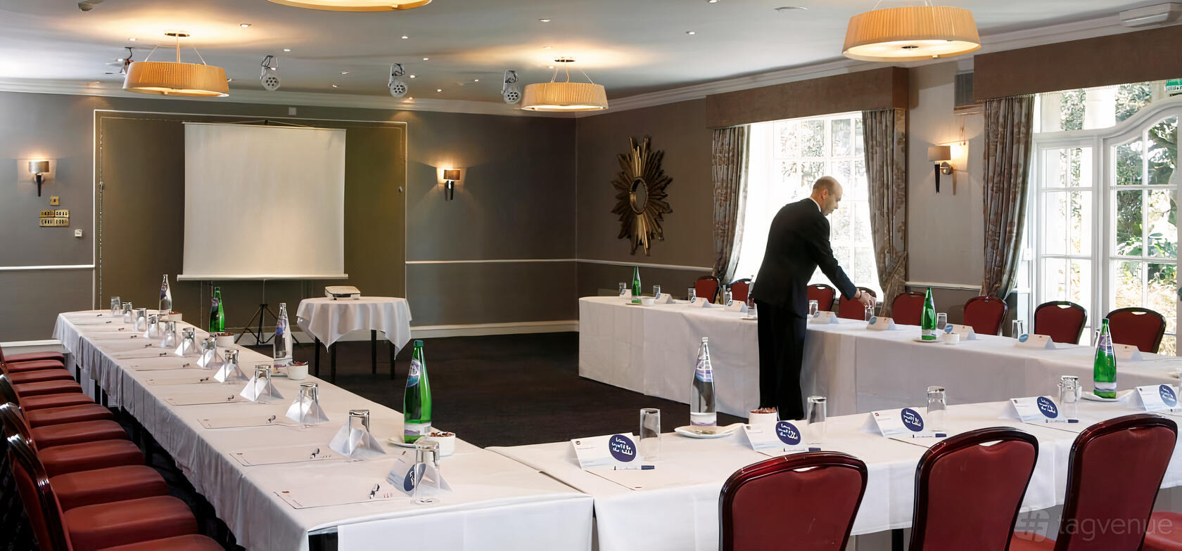 An event space with U-shaped tables, red chairs, paper name cards, and a projector screen at Keavil House Hotel.