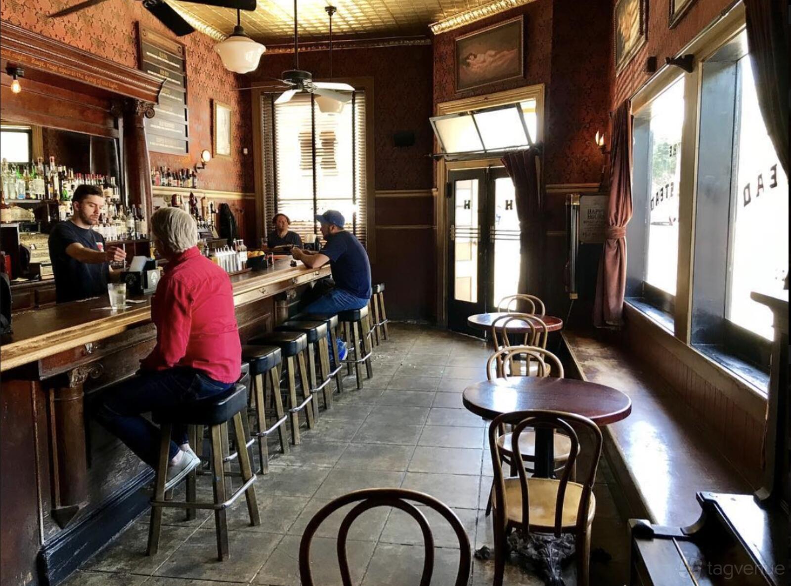 A bar with wooden stools, vintage wallpaper, large windows, and high ceilings at The Homestead.