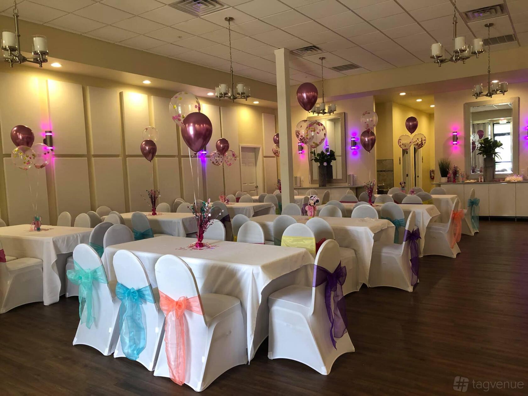 An event venue with decorated round and rectangular tables, white chair covers, and colorful balloon centerpieces at Suites of Keller.