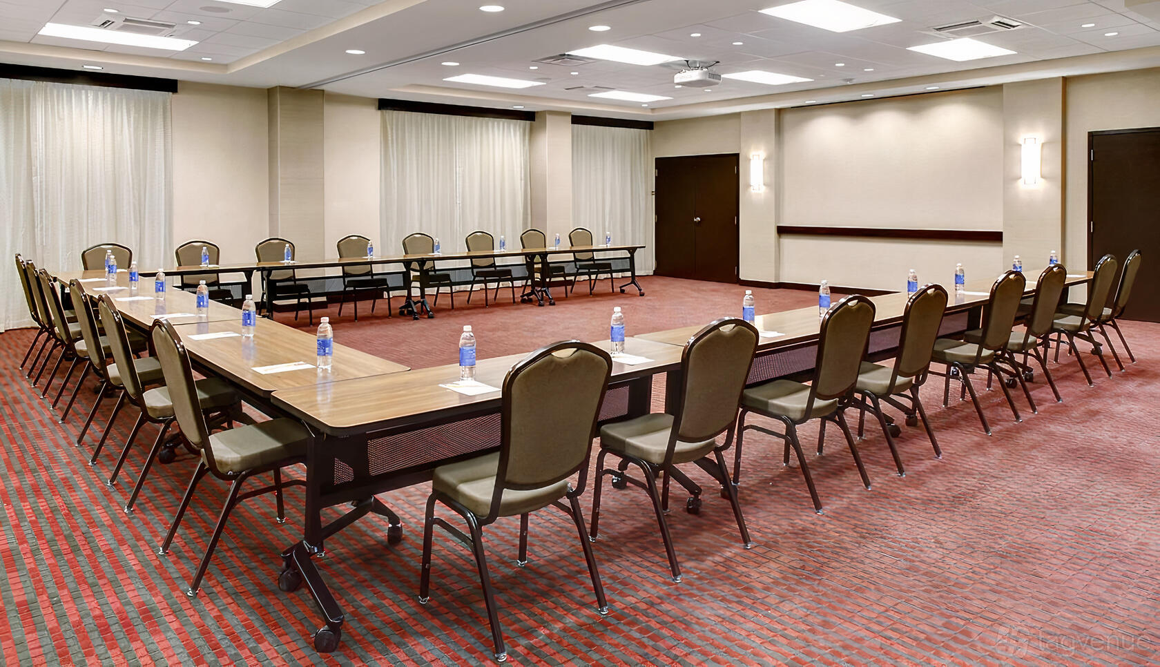 An event space with U-shaped tables, cushioned chairs, and bottled water at Hyatt Place Dallas North Galleria.