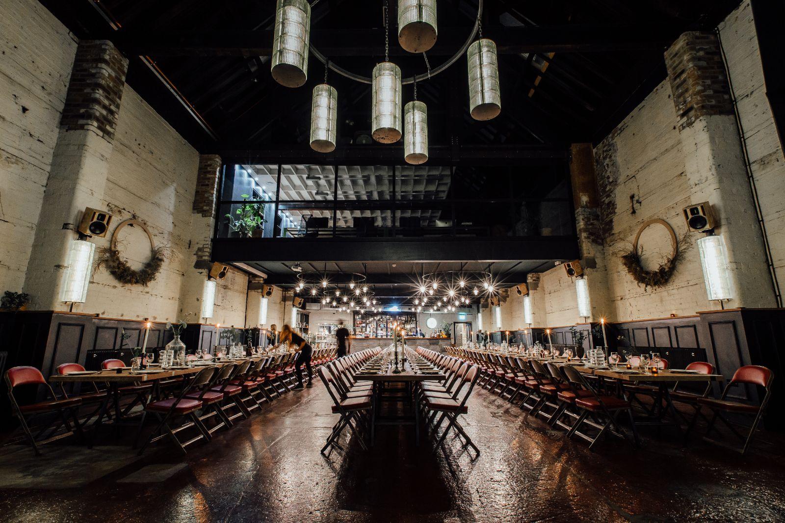 An event venue with high ceilings, exposed brick walls, and long banquet tables set with glassware at The Mowbray.