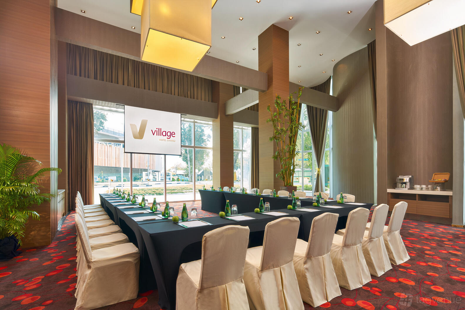 An event space with floor-to-ceiling windows, U-shaped tables, and greenery at Village Hotel Changi.