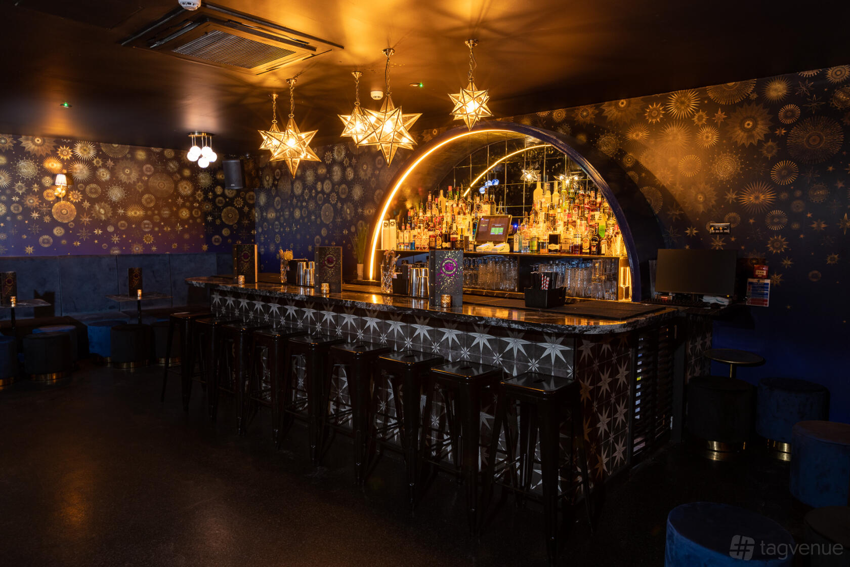 A cocktail bar with star-shaped pendant lights, mirrored back bar, and patterned blue walls at The Cocktail Club Birmingham.