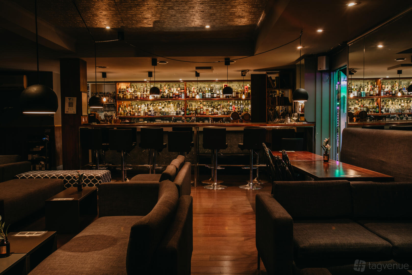 A pub with dark wood floors, lounge seating, and a backlit bar lined with bottles at East Of Everything.