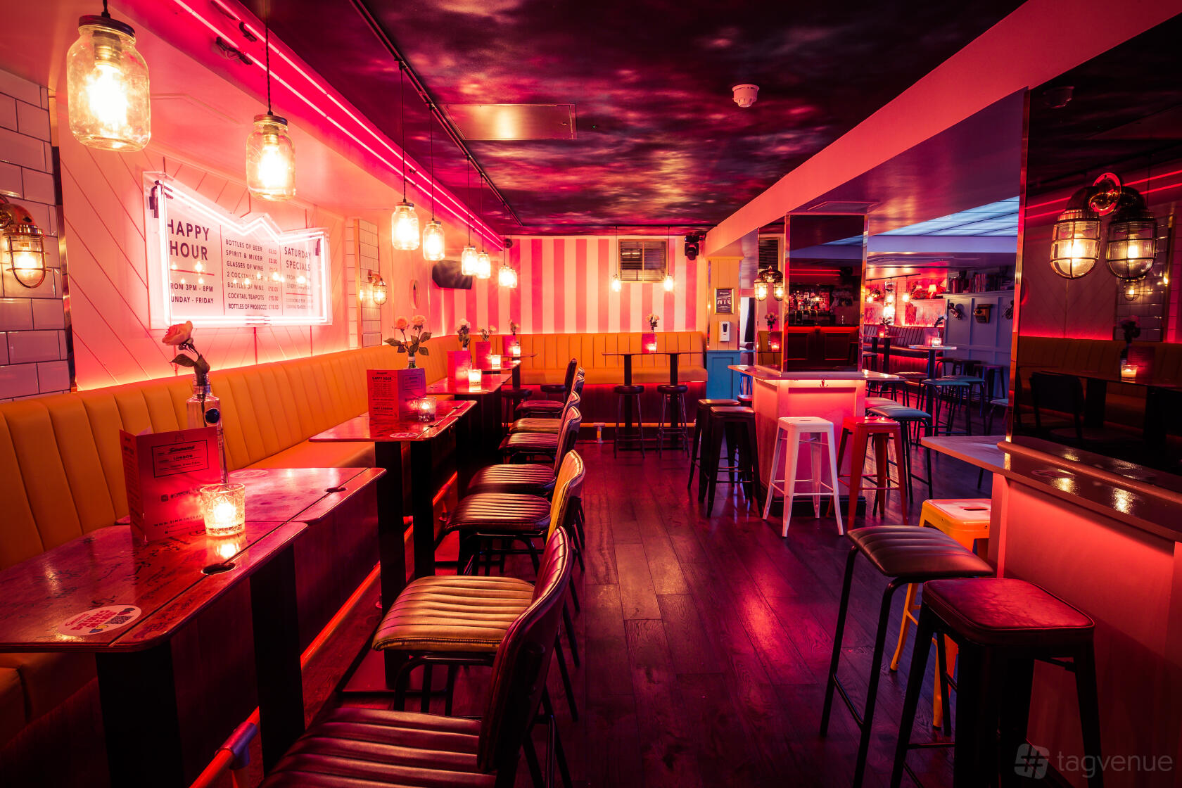 A bar with neon lighting, high tables with stools, and exposed bulbs at Simmons | Leicester Square.