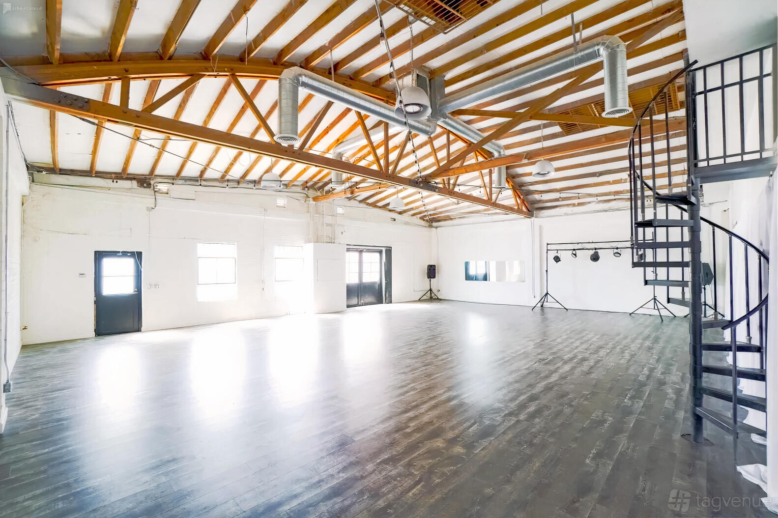 A loft with exposed wooden beams, high ceilings, natural light, and a spiral staircase at The Industry Loft.