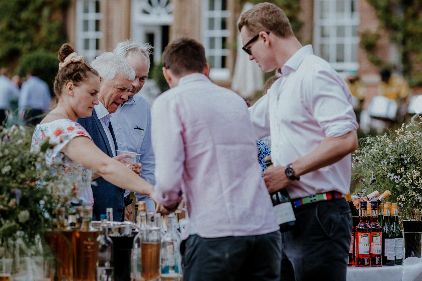 An outdoor drinks reception with guests gathered around a table with assorted bottles at Norwood Park Country House.