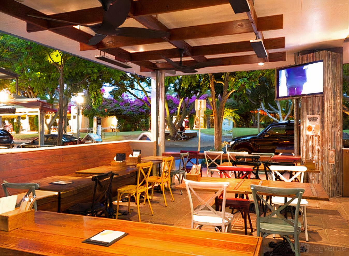 An open-air bar area with wooden tables, mixed-color chairs, ceiling fans, and street views at Barbossa Bar.