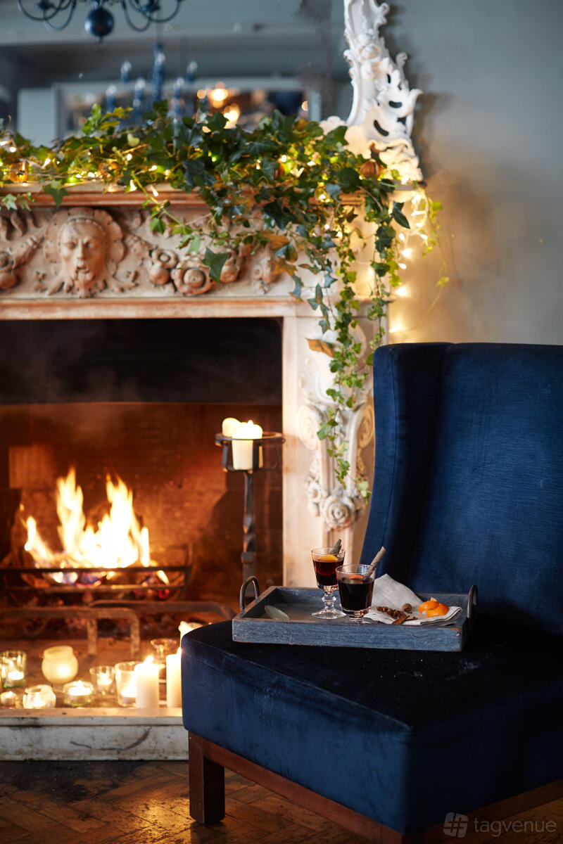 A function room in a pub with a carved stone fireplace, burning fire, ivy, and candles at Duke's Head Putney.