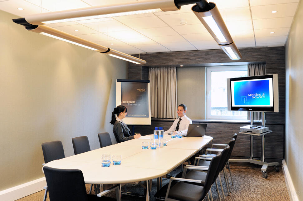 An event space with a long conference table, black chairs, and a wall-mounted screen at Novotel London Waterloo.
